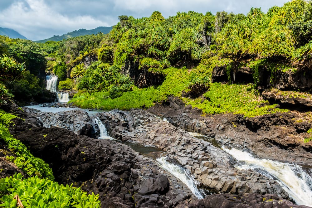 Several waterfalls cascade into pools (called the Seven Sacred Pools) on one of the best hikes in Maui, with lush greenery surrounding it.