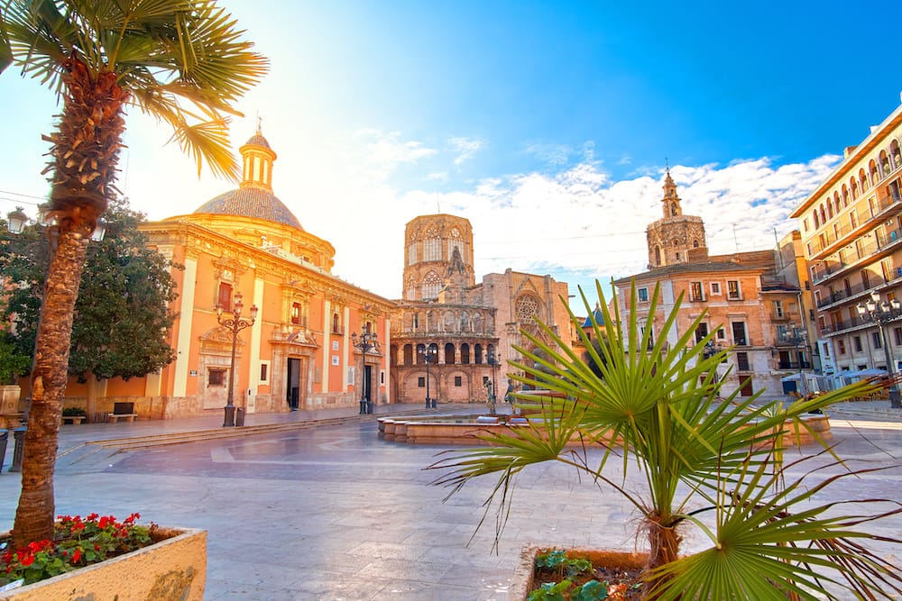 The Jewish Quarter in Valencia with historic buildings, palm trees and greenery, and a cloudy blue sky. This is one of the best places to visit in Spain in spring