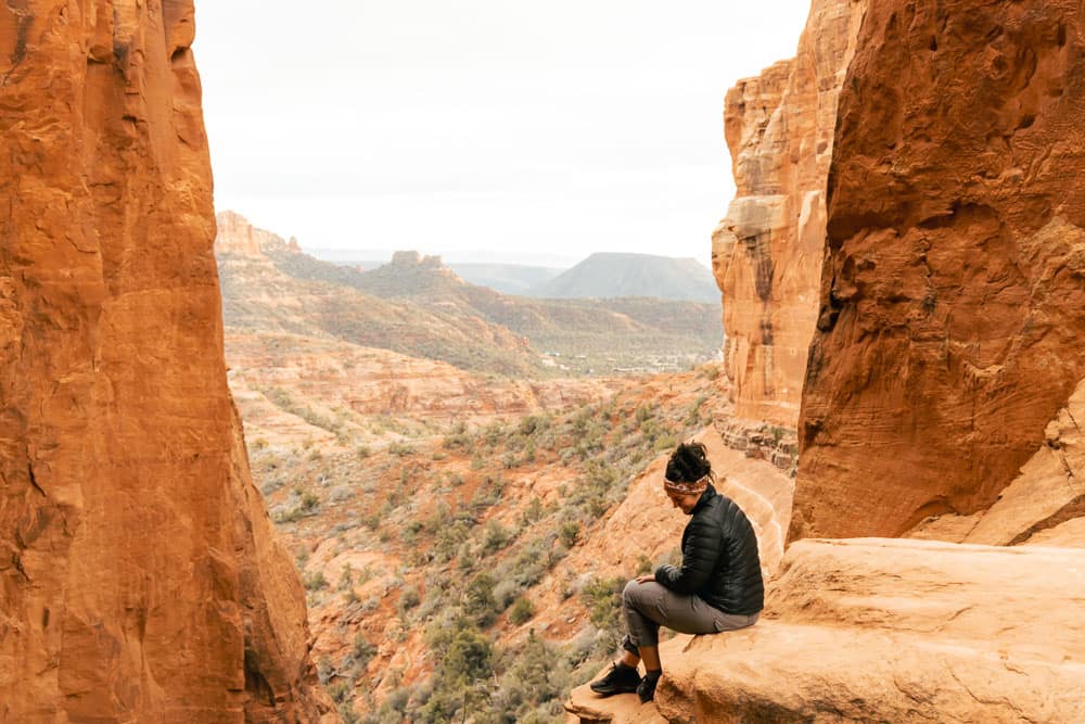 A woman sitting on the edge of a red rock at one of the best Instagram spots in Sedona.