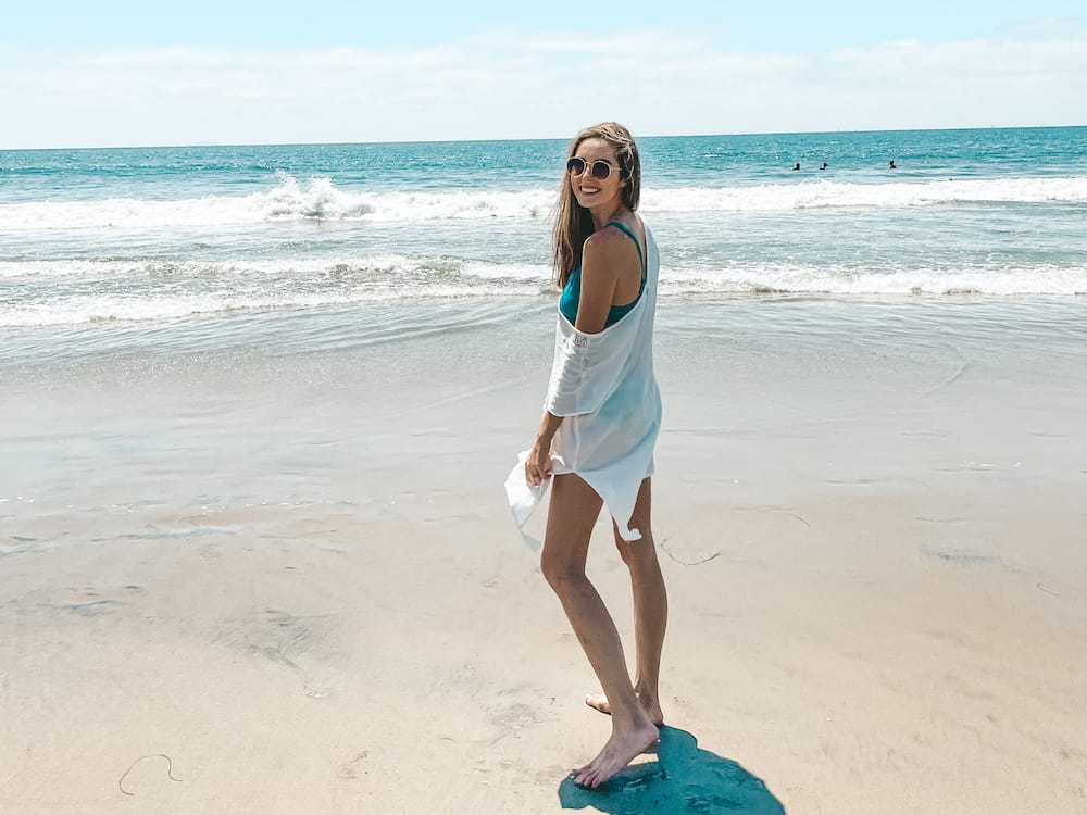 A girl wearing a green swimsuit and a white dress standing on a sandy beach in California