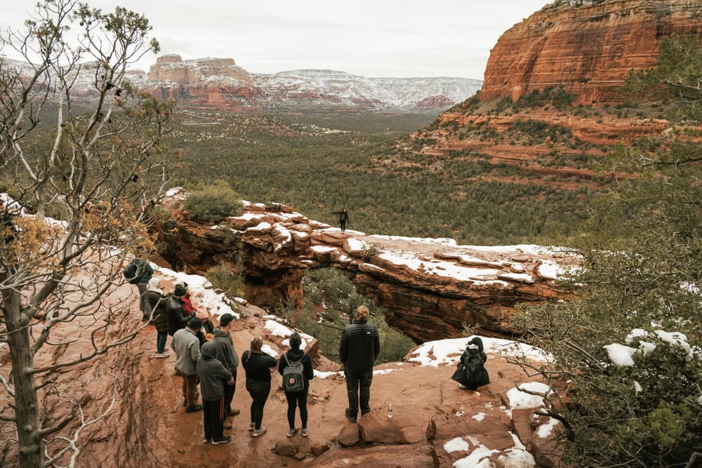 Several people standing and looking at Devil's Bridge, one of the best Sedona Instagram spots, in the snow.