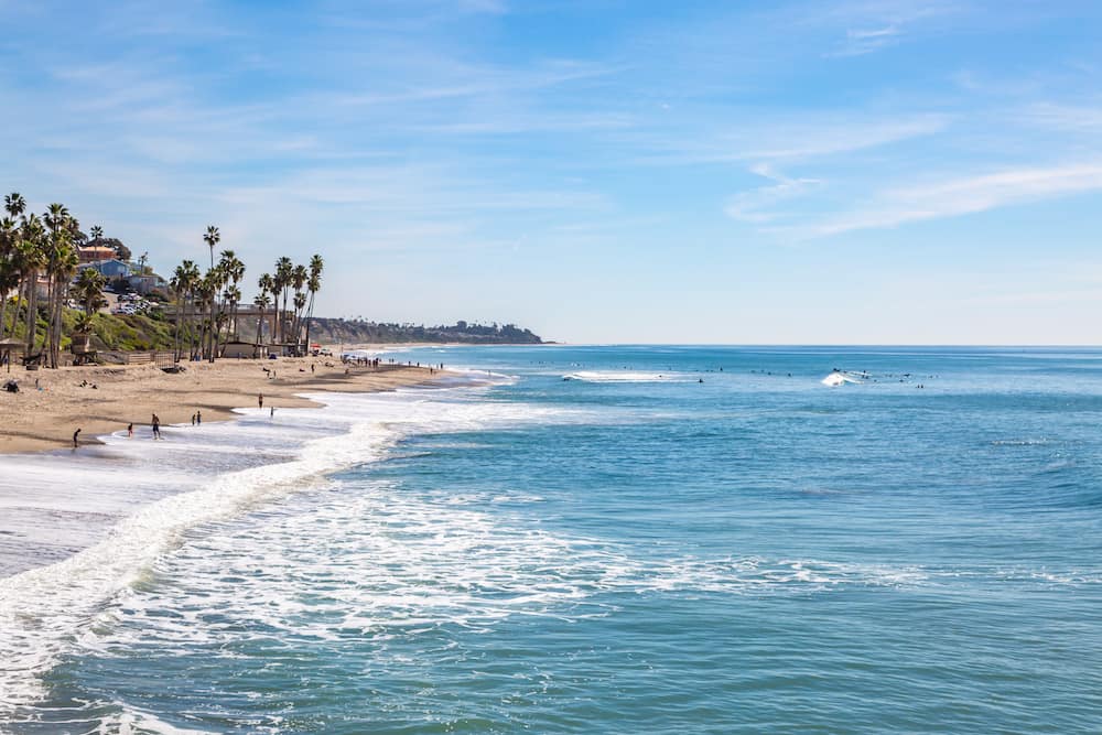 Blue ocean waves lapping onto a golden sand beach framed with palm trees in San Clemente, one of the best beaches in California