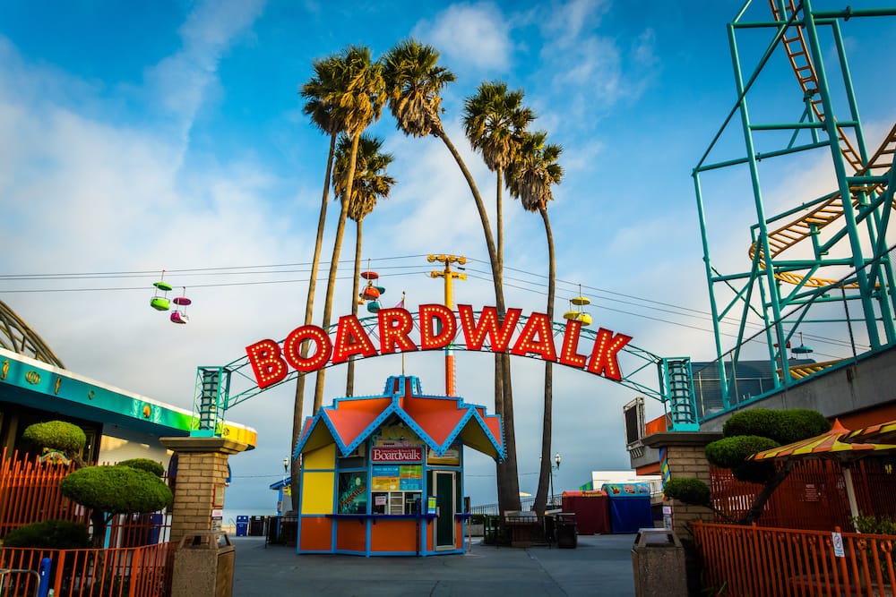 A colorful boardwalk on a beach in California with roller coasters and amusement park rides